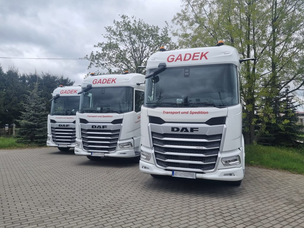 Trzy ciągniki siodłowe firmy GADEK zaparkowane przed bazą – nowoczesna flota transportowa.